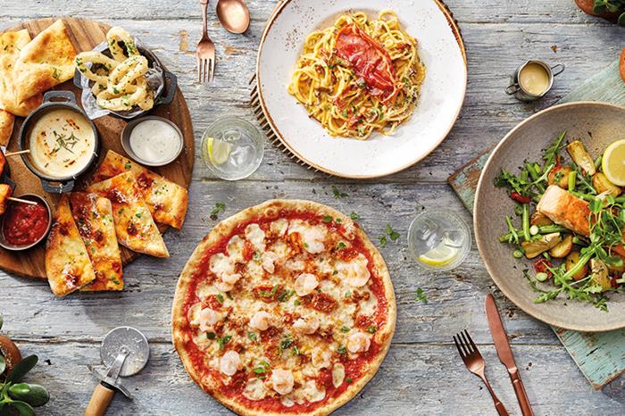 Italian food on dishes on a wooden table at Zizzi including pizza and pasta