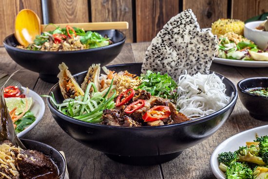 Picture of a noodle bowl with dragonfruit and chilli on a wooden table with other bowls