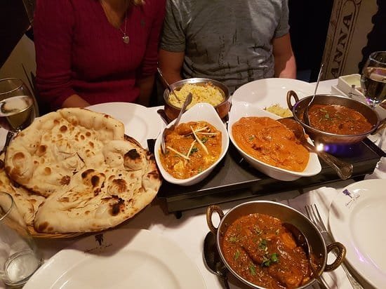 Picture of curries in white boats and a metal bowl with a large naan