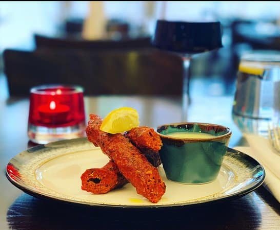 Picture of fritters stacked standing against each other one a plate with a slice of lemon and a dipping sauce