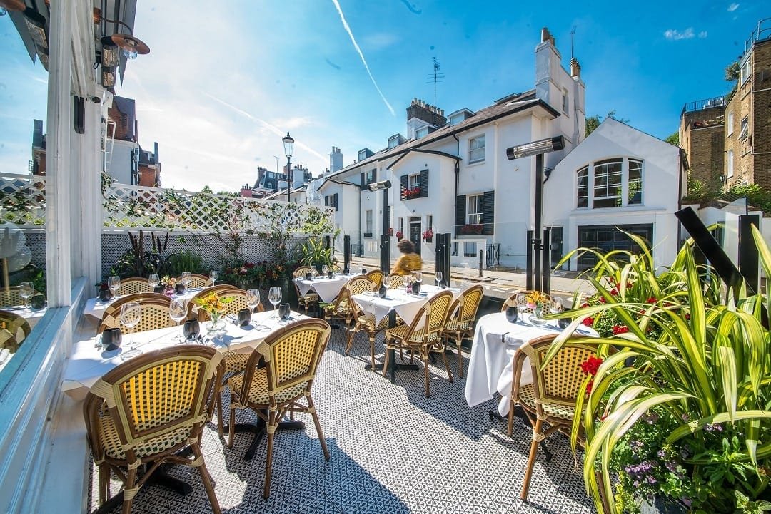 Picture of the outside patio of Chakra restaurant on a sunny day with white table-cloths and buildings visible across the road