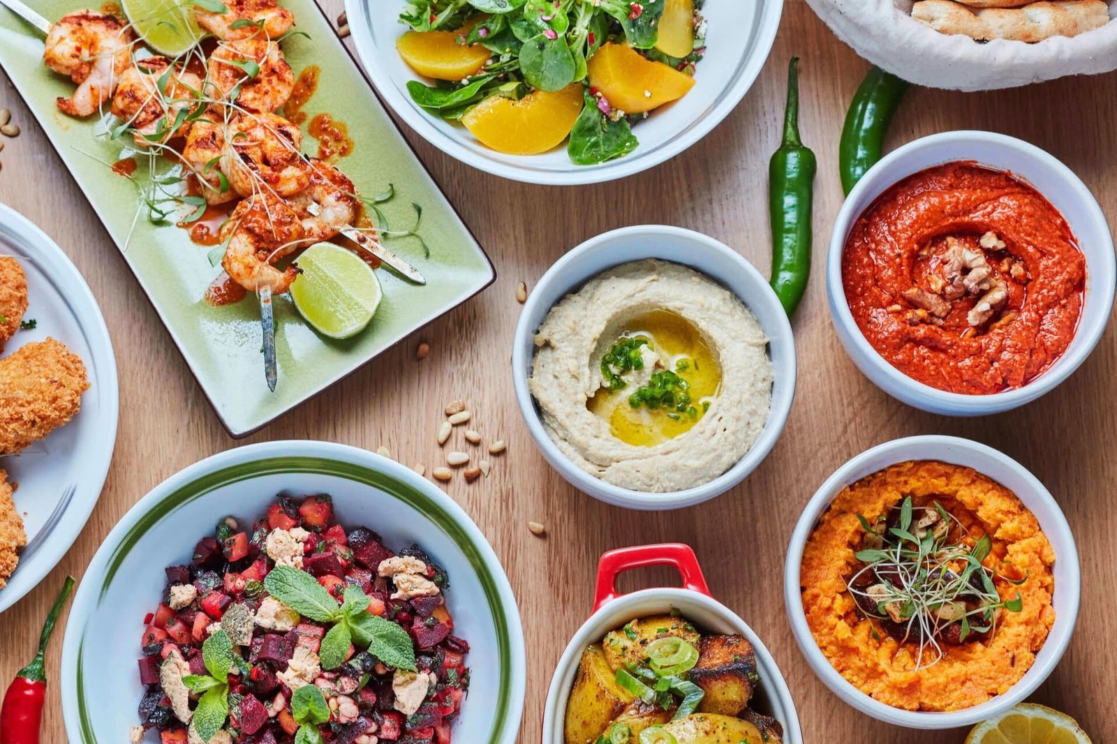 Table filled with bowls of food from Ceru like hummus and dips with chillies and nuts on a wooden table